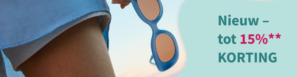 Lachende vrouw met een witte zonnebril in zomerse kleding zit in het groen.