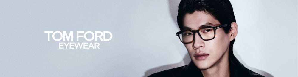 Man met een havanna-bril, staand naast de tekst \'Tom Ford Eyewear\' op een lichte achtergrond.