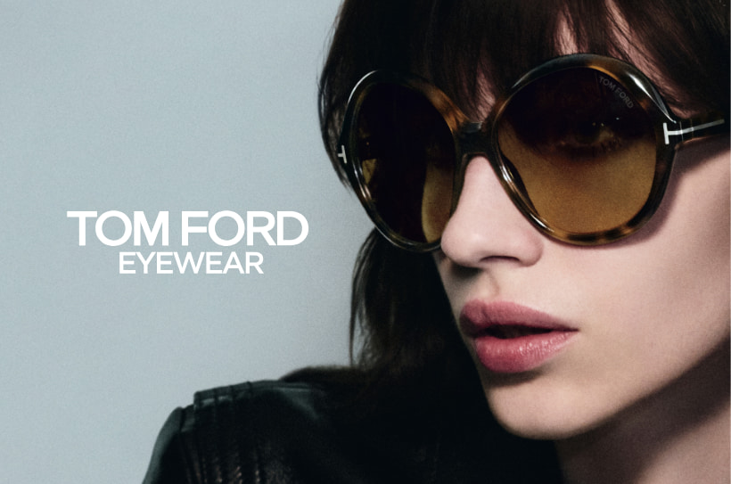 Femme portant des lunettes de soleil Tom Ford rondes et marron, avec une veste en cuir noire, sur un fond gris ; à gauche de l’image, le logo « TOM FORD EYEWEAR ».