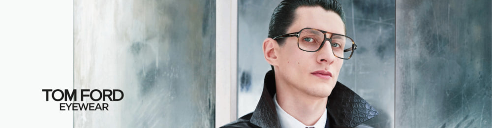 Homme portant des lunettes Tom Ford, vêtu d’un manteau en cuir et d’une cravate, devant un fond moderne.
