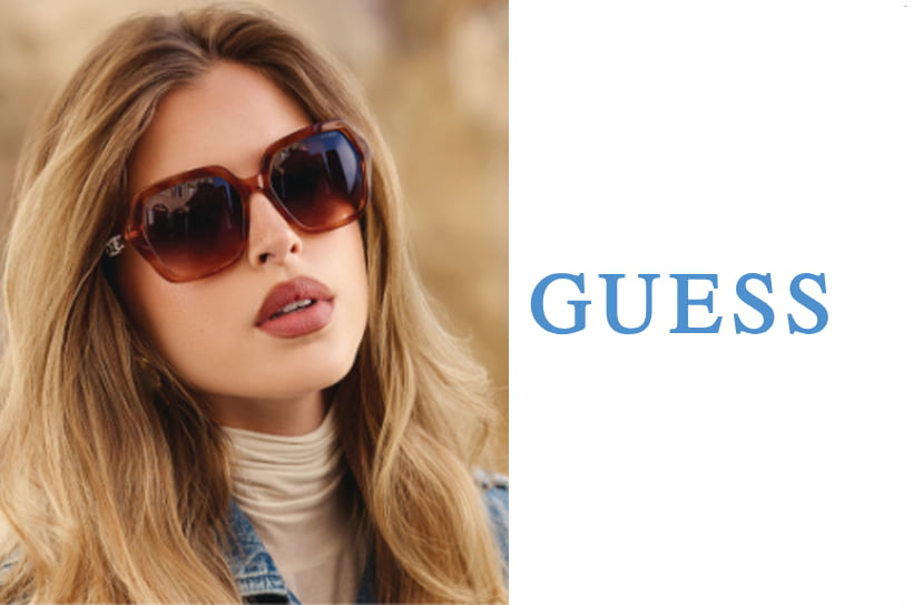 Vrouw met lange blonde haren en grote bruine Guess-zonnebril, stijlvolle look in buitenomgeving.
