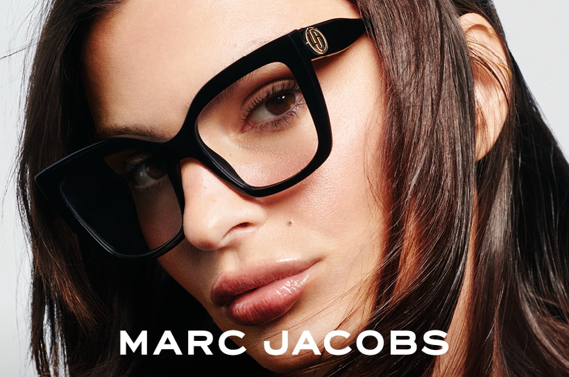 Gros plan d’une femme portant des lunettes noires Marc Jacobs à la forme cat-eye marquée ; logo MJ doré sur la monture.
