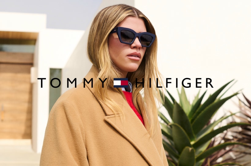 Vrouw met blond haar draagt een zwarte zonnebril. Logo Tommy Hilfiger zichtbaar.
