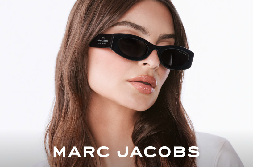 Femme aux longs cheveux bruns portant des lunettes de soleil noires et fines de Marc Jacobs.