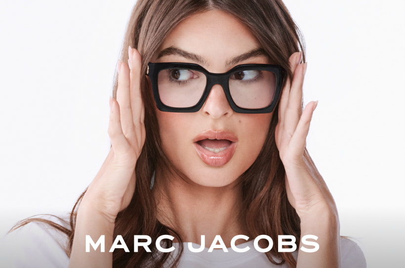 Vrouw met lang bruin haar draagt een grote zwarte bril van Marc Jacobs en houdt beide handen tegen het montuur.