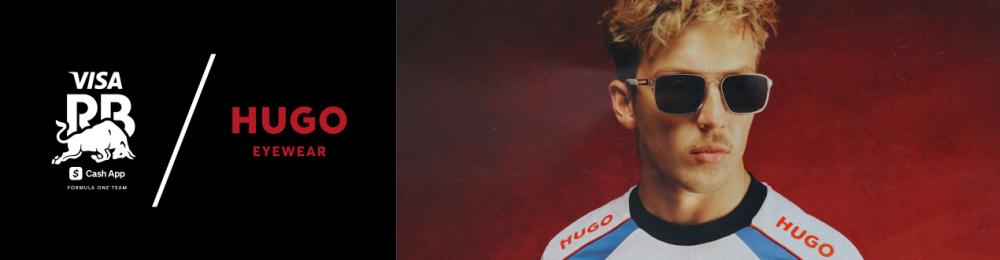 Man met kort blond haar draagt een rechthoekige zonnebril van HUGO Eyewear en een sportshirt met sponsorenlogo’s.
