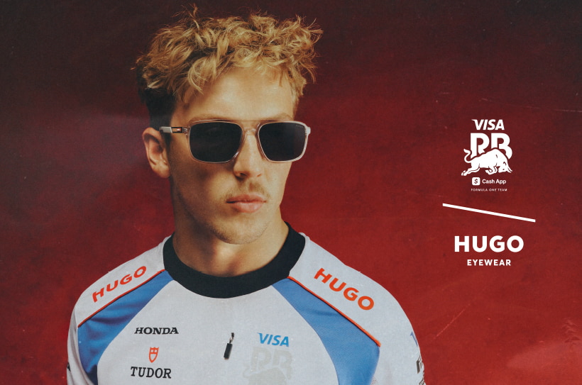 Man met kort blond haar draagt een rechthoekige zonnebril van HUGO Eyewear en een sportshirt met sponsorenlogo’s.