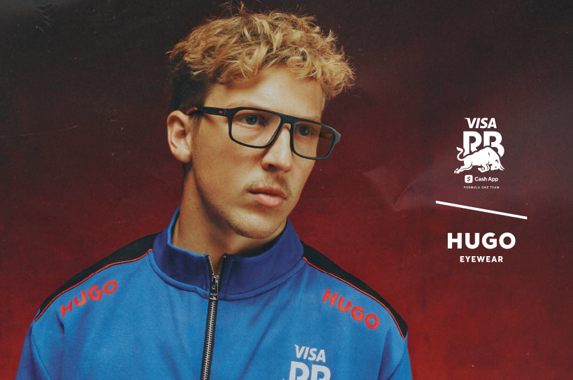Homme aux cheveux blonds courts portant des lunettes rectangulaires HUGO Eyewear et une veste de sport bleue avec logos de sponsors.