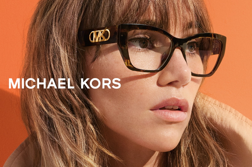 Vrouw met grote Michael Kors bril met goud logo, oranje achtergrond.
