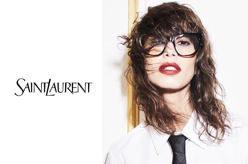 Femme avec lunettes cat-eye Saint Laurent, rouge à lèvres et chemise blanche ; logo à gauche.