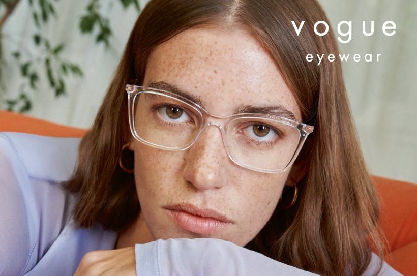 Femme portant des lunettes Vogue transparentes et un haut lilas clair, regardant droit vers la caméra.