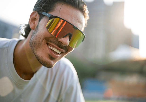 Man met sportieve Chamelo-zonnebril met spiegelglas, lachend in de zon.