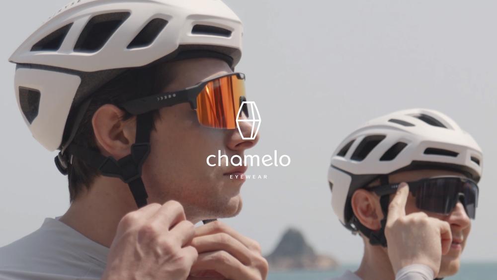 Twee fietsers met witte helmen dragen Chamelo zonnebrillen, klaar voor een rit, met Chamelo-logo in het midden.