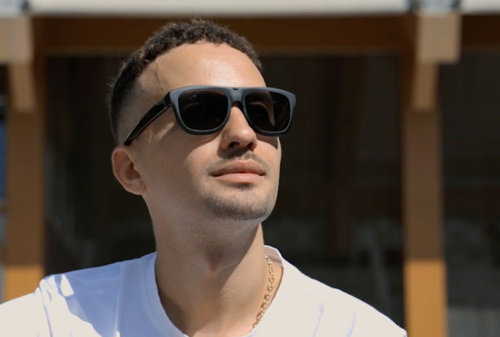 Man met zonnebril en wit T-shirt kijkt omhoog in de zon.