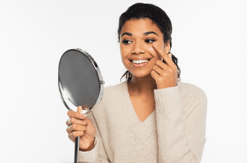 Vrouw glimlacht terwijl ze in de spiegel kijkt en een contactlens inzet.