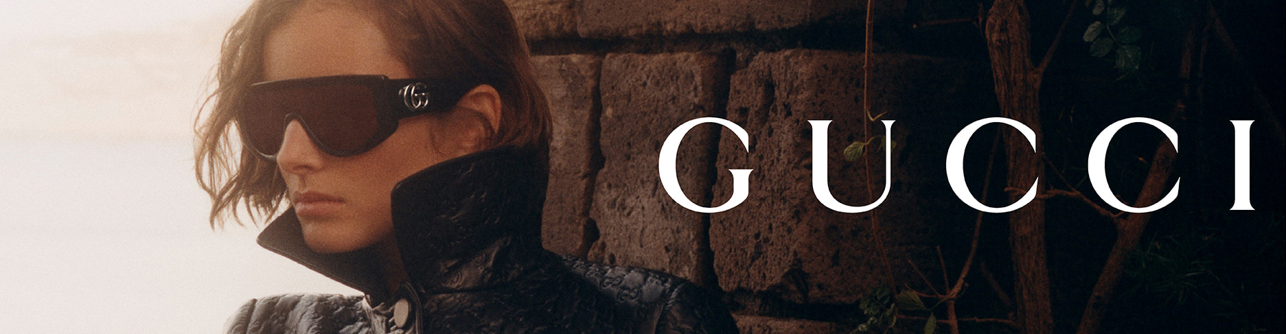 Mannequin en manteau Gucci noir et lunettes logo, ambiance luxueuse face à la mer.