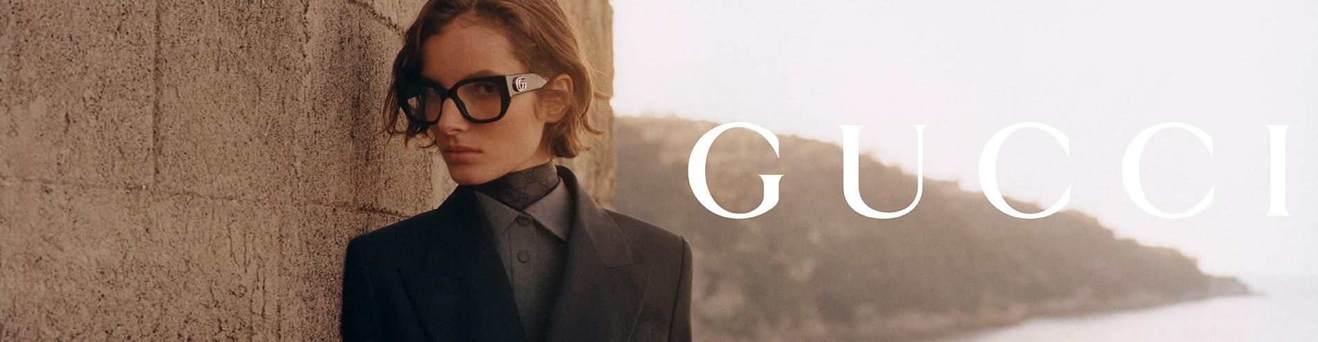 Model met zwarte Gucci-bril en pak, stijlvolle luxe uitstraling bij stenen muur.