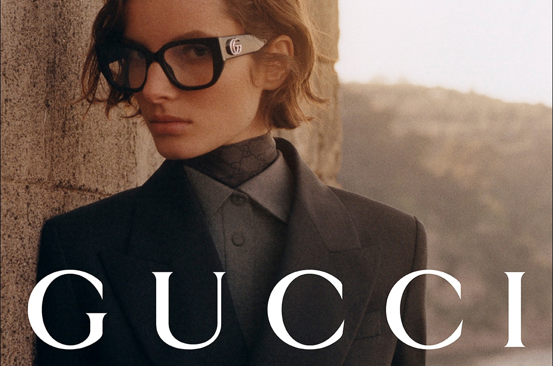 Model met zwarte Gucci-bril en pak, stijlvolle luxe uitstraling bij stenen muur.