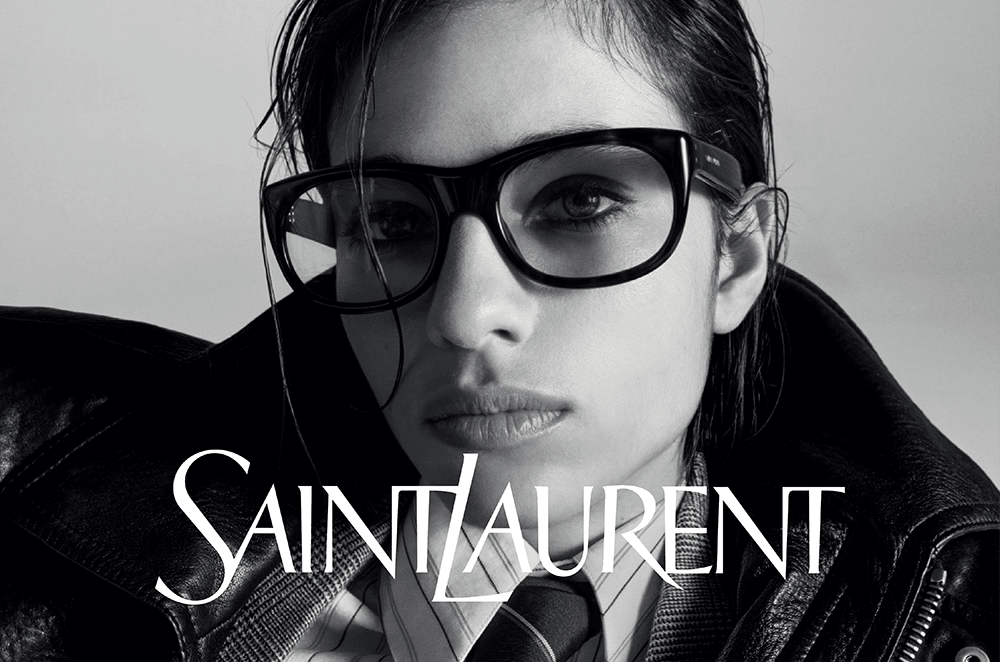 Model met zwarte Saint Laurent-bril, leren jas en stropdas in zwart-wit portret.