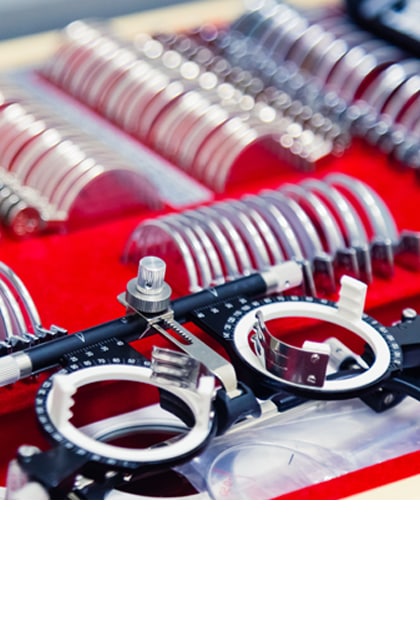 Een set met proefbrillen en verschillende correctielenzen, gebruikt voor oogonderzoeken. De lenzen zijn gesorteerd in een rode koffer, met twee zwarte proefbrilmonturen op de voorgrond.