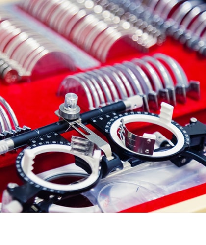 Een set met proefbrillen en verschillende correctielenzen, gebruikt voor oogonderzoeken. De lenzen zijn gesorteerd in een rode koffer, met twee zwarte proefbrilmonturen op de voorgrond.