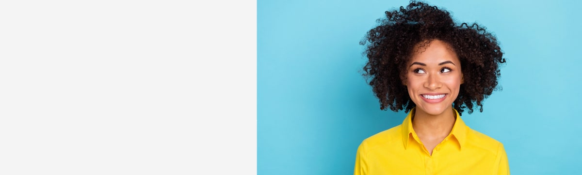 Vrouw met krullend haar en een geel hemd glimlacht en kijkt opzij voor een blauwe achtergrond.