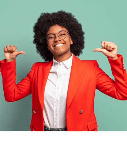 Een vrolijk lachende vrouw met krullend donker haar en een bril wijst met beide duimen naar zichzelf. Ze draagt een rode blazer over een witte blouse en staat voor een mintgroene achtergrond.