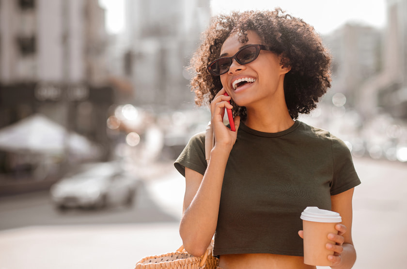 Lachende vrouw met zonnebril aan de telefoon met koffie.