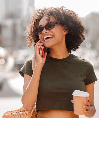 Lachende vrouw met zonnebril aan de telefoon met koffie.