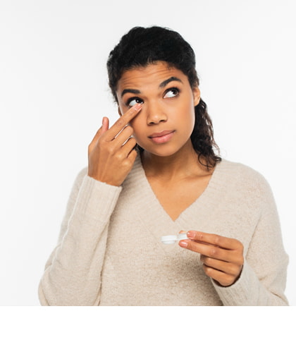 Een vrouw zet een contactlens in haar oog terwijl ze in de spiegel kijkt in een lichte badkamer.