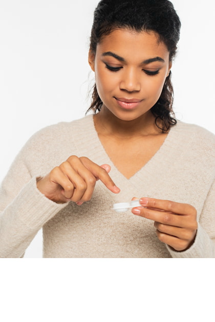 Een persoon wast zijn handen bij een wastafel met een zwarte kraan, op de achtergrond staan tandenborstels in een beker. Op de wastafel ligt een contactlenshouder.